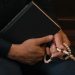 Close-up of hands holding prayer beads and book, symbolizing faith and spirituality.