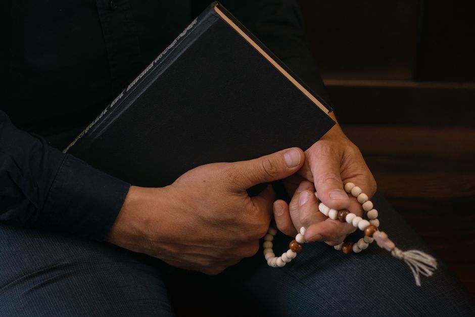 Close-up of hands holding prayer beads and book, symbolizing faith and spirituality.