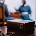 A close-up of a Holy Bible and prayer beads on a wooden table with blurred people in background.
