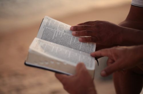 Close-up of hands holding an open Bible on a beach, symbolizing faith and study.