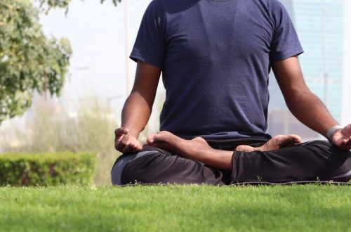 A man practicing meditation in lotus pose on a sunny day in an outdoor urban park.