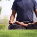 A man practicing meditation in lotus pose on a sunny day in an outdoor urban park.