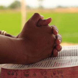 Close-up of hands clasped in prayer over an open Bible, symbolizing faith and devotion.