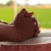Close-up of hands clasped in prayer over an open Bible, symbolizing faith and devotion.