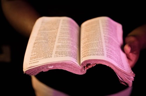 An open Bible held in hands with dramatic lighting, creating a serene atmosphere.