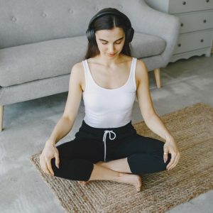 Woman meditating indoors on a rug with headphones, promoting relaxation and wellness.