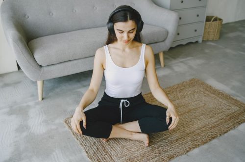 Woman meditating indoors on a rug with headphones, promoting relaxation and wellness.