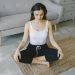 Woman meditating indoors on a rug with headphones, promoting relaxation and wellness.