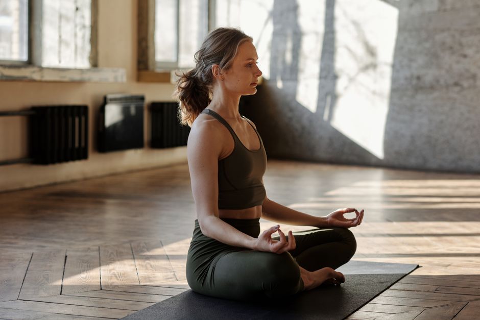 A woman meditates in a peaceful yoga pose indoors, embracing wellness and relaxation.