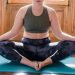 A woman in a relaxed lotus position doing yoga inside a cozy home space.