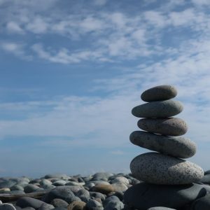 A tranquil scene of a balanced stone stack on a pebble beach under a bright blue sky.