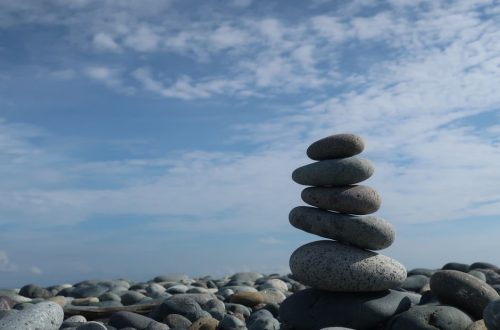 A tranquil scene of a balanced stone stack on a pebble beach under a bright blue sky.