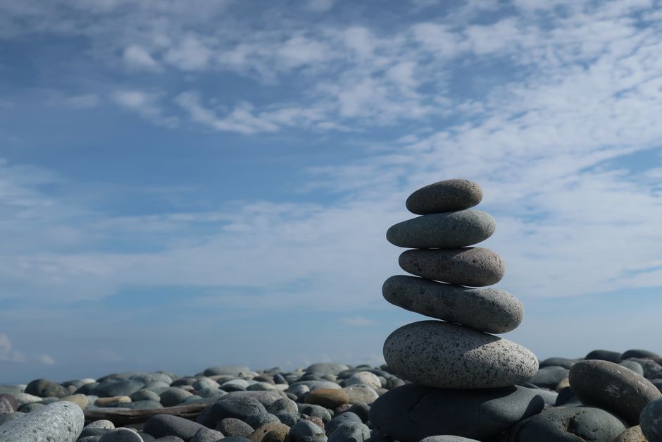 A tranquil scene of a balanced stone stack on a pebble beach under a bright blue sky.