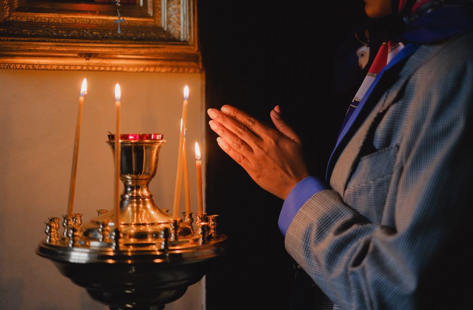 A person praying beside lit candles in a religious setting, evoking peace and spirituality.