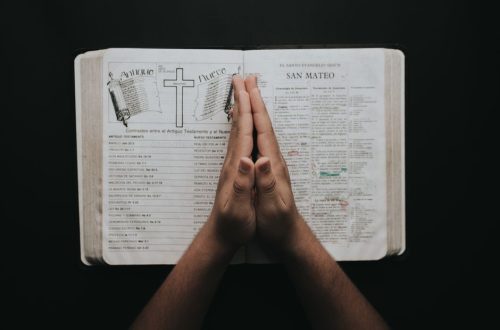 Hands clasped in prayer on an open Bible showing the book of Matthew, emphasizing faith and spirituality.