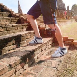 A tourist wearing sneakers climbs ancient brick steps at a historic temple site on a sunny day.