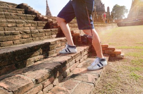 A tourist wearing sneakers climbs ancient brick steps at a historic temple site on a sunny day.