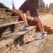 A tourist wearing sneakers climbs ancient brick steps at a historic temple site on a sunny day.