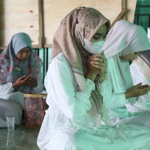 A group of women in hijabs kneeling indoors, focused on prayer and spirituality.