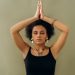 A woman in a black top meditates with closed eyes and hands in prayer pose, radiating calmness.