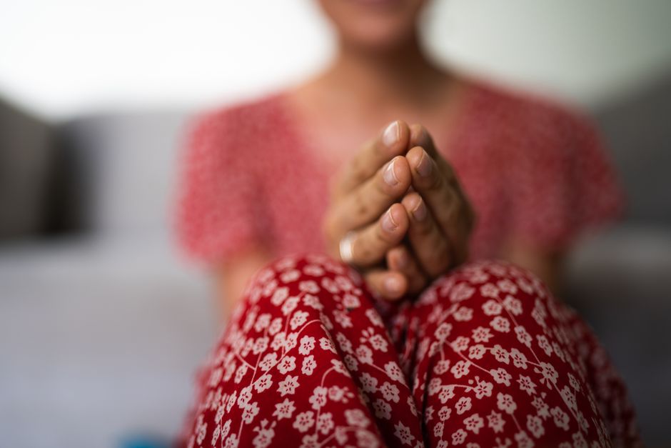 Close-up of a person in a floral dress with hands in prayer, soft focus.