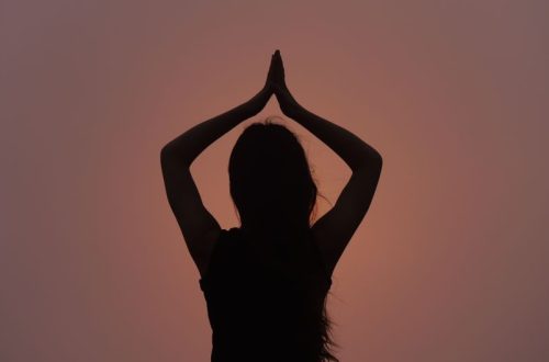 Silhouette of a woman in a yoga pose against a sunset sky, symbolizing peace and meditation.