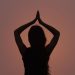 Silhouette of a woman in a yoga pose against a sunset sky, symbolizing peace and meditation.