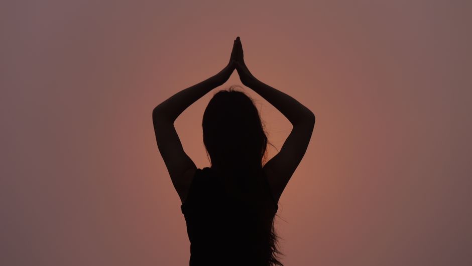 Silhouette of a woman in a yoga pose against a sunset sky, symbolizing peace and meditation.