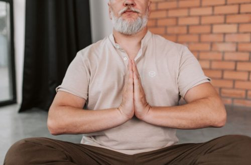 Senior man practicing meditation with hands in prayer pose inside a calm setting.