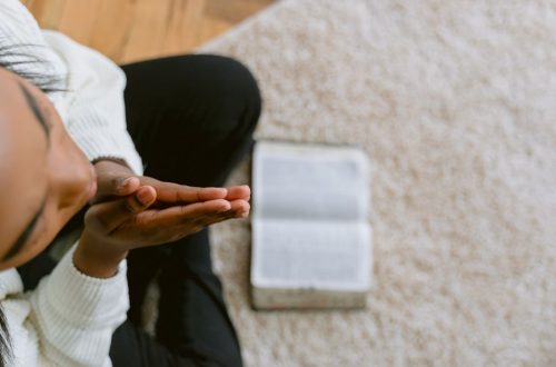 High angle view of a woman in prayer with an open Bible, symbolizing devotion and faith.