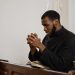 A thoughtful man in a church pew praying with hands clasped and eyes closed.