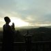 A monk in silhouette prays peacefully at sunrise with mountains in the background.