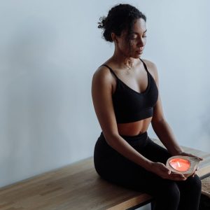 A woman in black activewear meditates with a candle, seated indoors for mindfulness and relaxation.