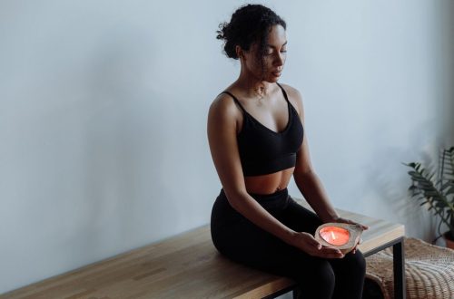 A woman in black activewear meditates with a candle, seated indoors for mindfulness and relaxation.