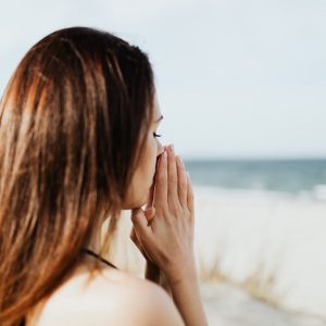 Woman meditating by the beach with hands together, embracing tranquility and peace.