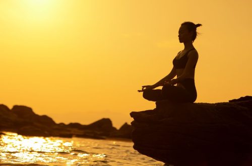 Woman practicing yoga in lotus pose on a cliff by the sea at sunset, embodying tranquility and balance.