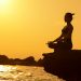 Woman practicing yoga in lotus pose on a cliff by the sea at sunset, embodying tranquility and balance.