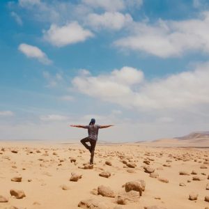 A man balancing in a serene yoga pose amidst the vast desert landscape of Huacachina, Peru.
