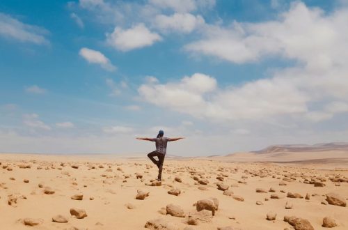 A man balancing in a serene yoga pose amidst the vast desert landscape of Huacachina, Peru.