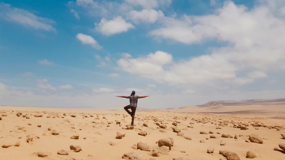 A man balancing in a serene yoga pose amidst the vast desert landscape of Huacachina, Peru.