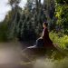 A woman in a traditional costume meditating on a rock amidst nature.