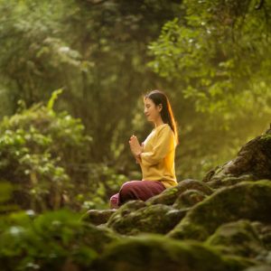 A woman meditates peacefully in a sunlit forest, embodying tranquility and connection with nature.