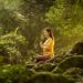 A woman meditates peacefully in a sunlit forest, embodying tranquility and connection with nature.