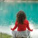 A woman in red meditates by a tranquil blue lake, reflecting calm and serenity.