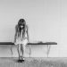 A black and white photo of a woman in thought, sitting on a bench indoors, portraying solitude.