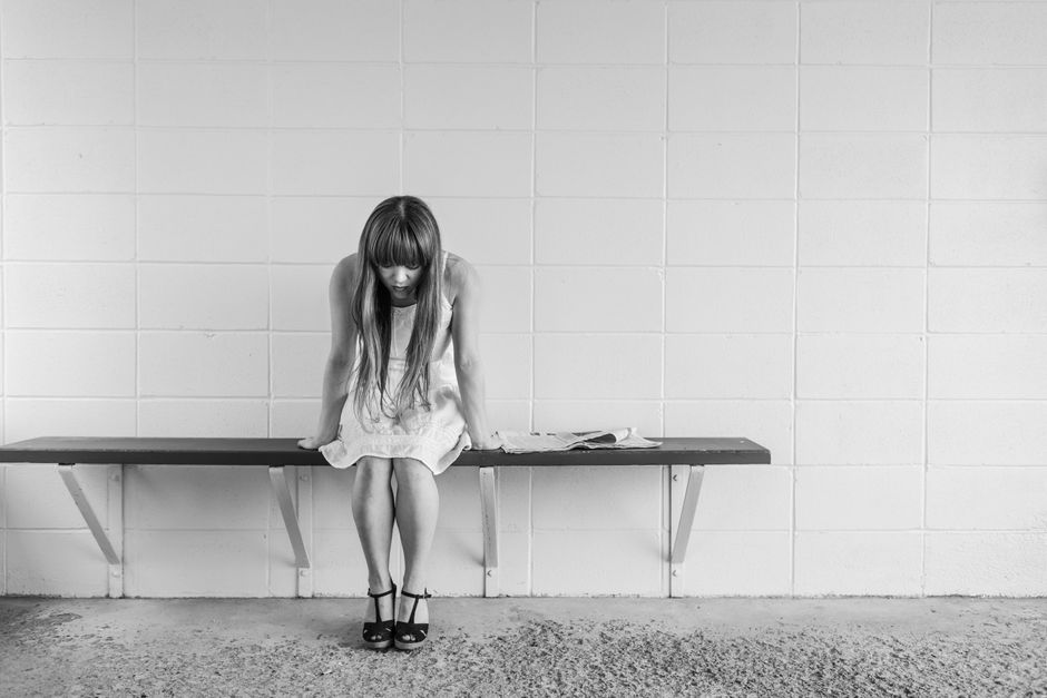 A black and white photo of a woman in thought, sitting on a bench indoors, portraying solitude.