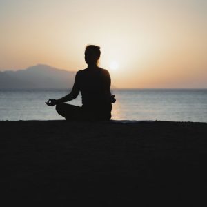 A woman practices meditation with a tranquil ocean sunset backdrop, embodying peace and relaxation.