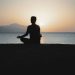 A woman practices meditation with a tranquil ocean sunset backdrop, embodying peace and relaxation.