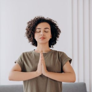 Young woman with curly hair meditates indoors, embracing tranquility and mindfulness.