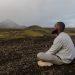 Man meditating on rocky terrain with mountain backdrop. Peace and tranquility outdoors.